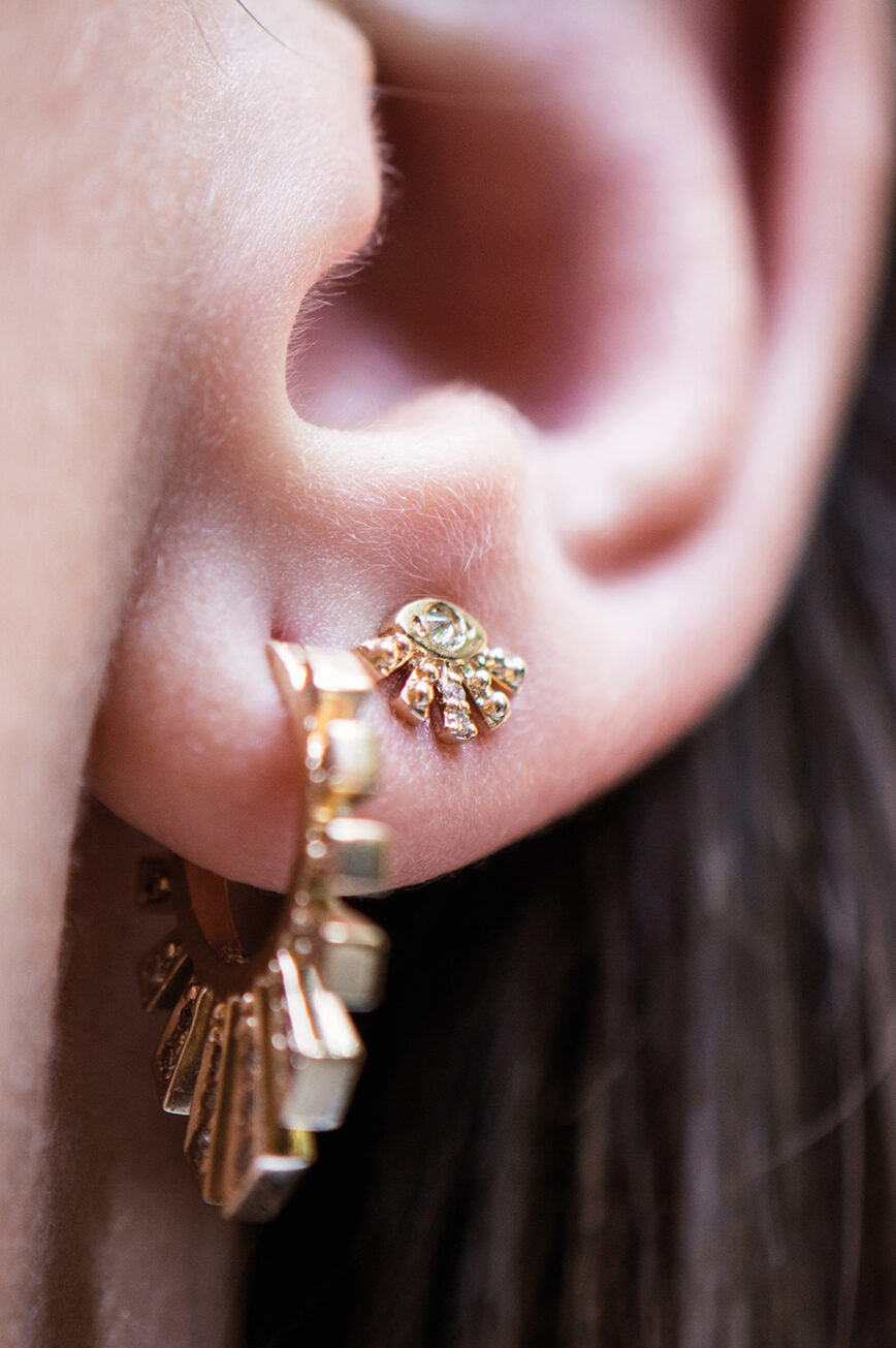 yellow gold stud earrings shaped as a small sunburst fan with a central diamond eye and radiating gold spikes, inspired by Aztec sun motifs