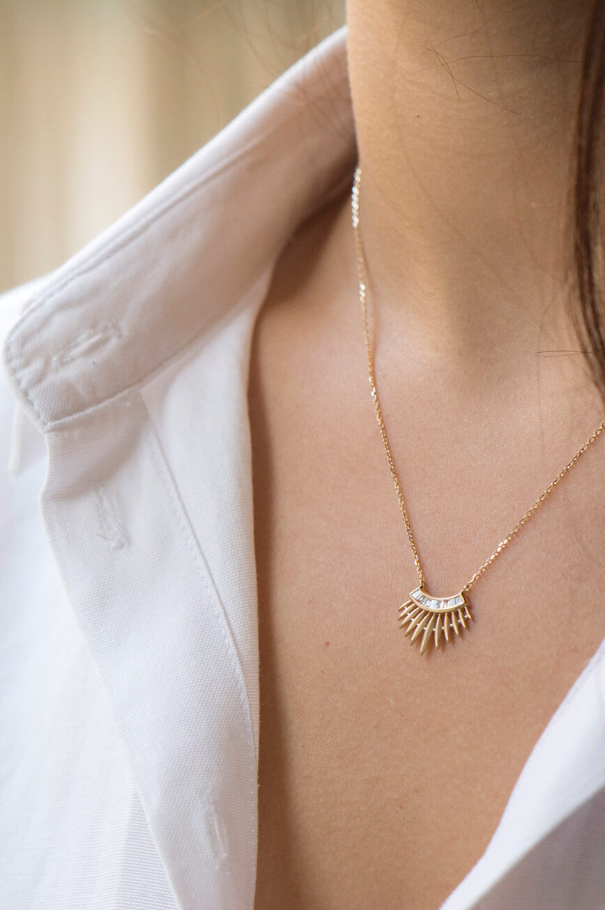 yellow gold necklace with a rising sun pendant composed of a row of baguette diamonds at center and radiating gold spike rays
