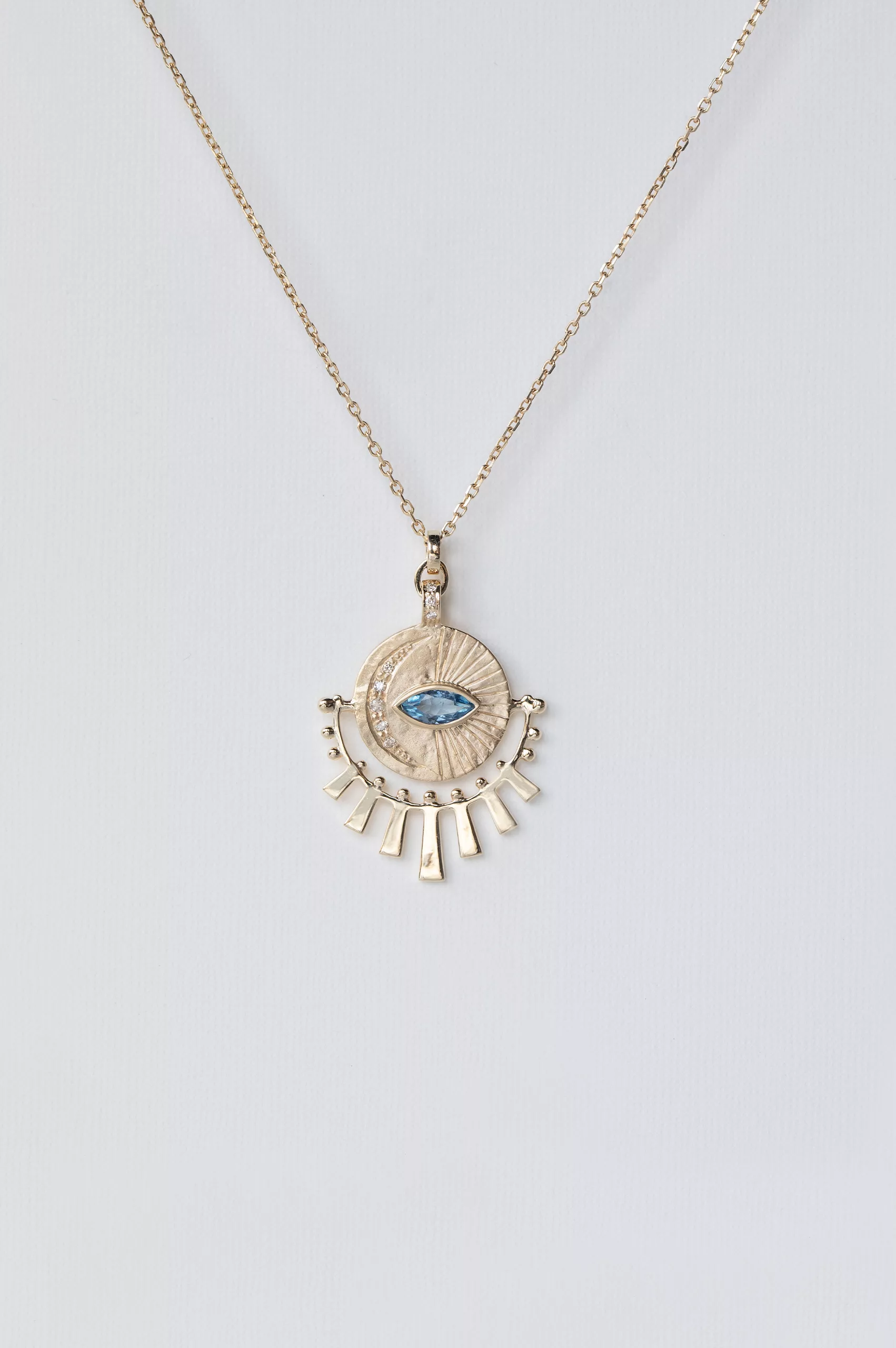 yellow gold necklace with a circular sunburst medal pendant featuring a central marquise aquamarine eye, surrounded by radiating gold sunbeams and small diamond accents