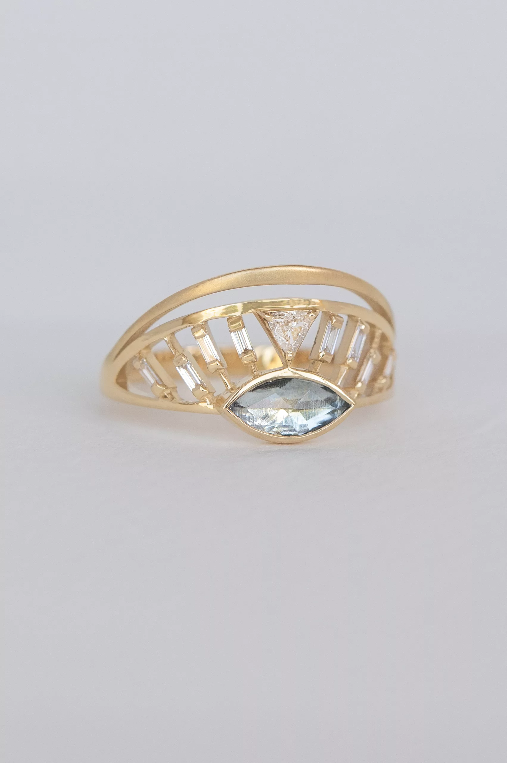 yellow gold architectural ring featuring a marquise-cut aquamarine at center flanked by baguette diamonds, set within an open cage-like crown structure