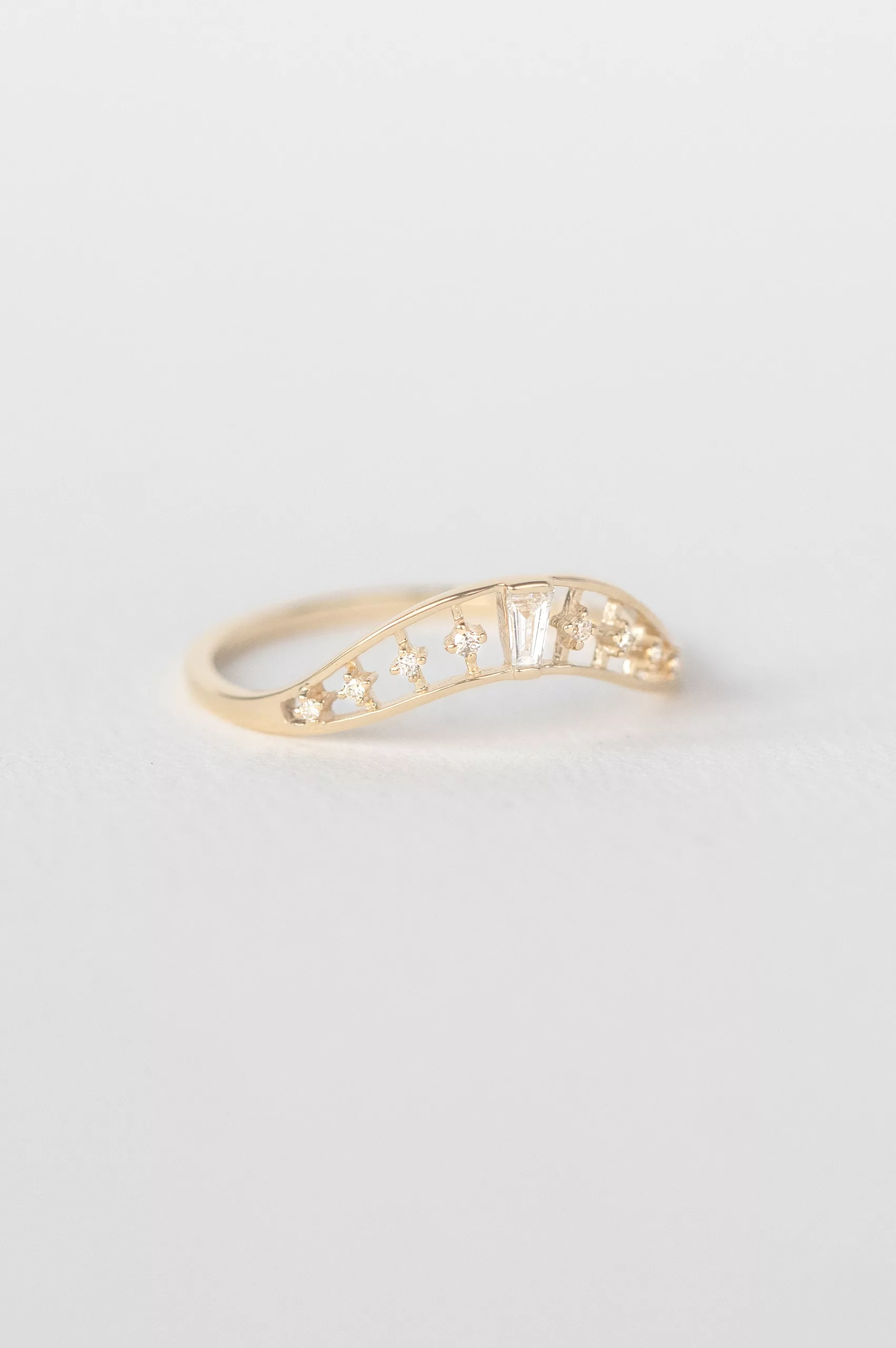 yellow gold curved ring featuring a baguette diamond at center flanked by round brilliant diamonds, set in a wave-shaped band
