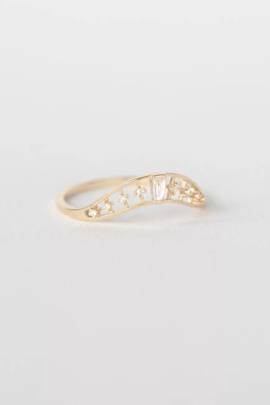 yellow gold curved ring featuring a baguette diamond at center flanked by round brilliant diamonds, set in a wave-shaped band