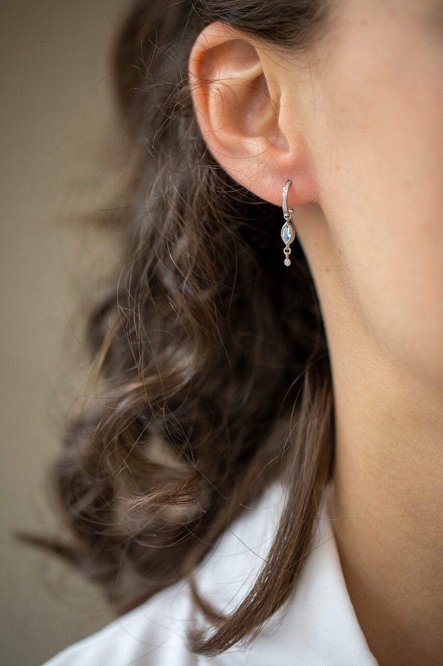 white gold single hoop earring with a pavé diamond hoop from which a marquise moonstone and three diamond drops are suspended