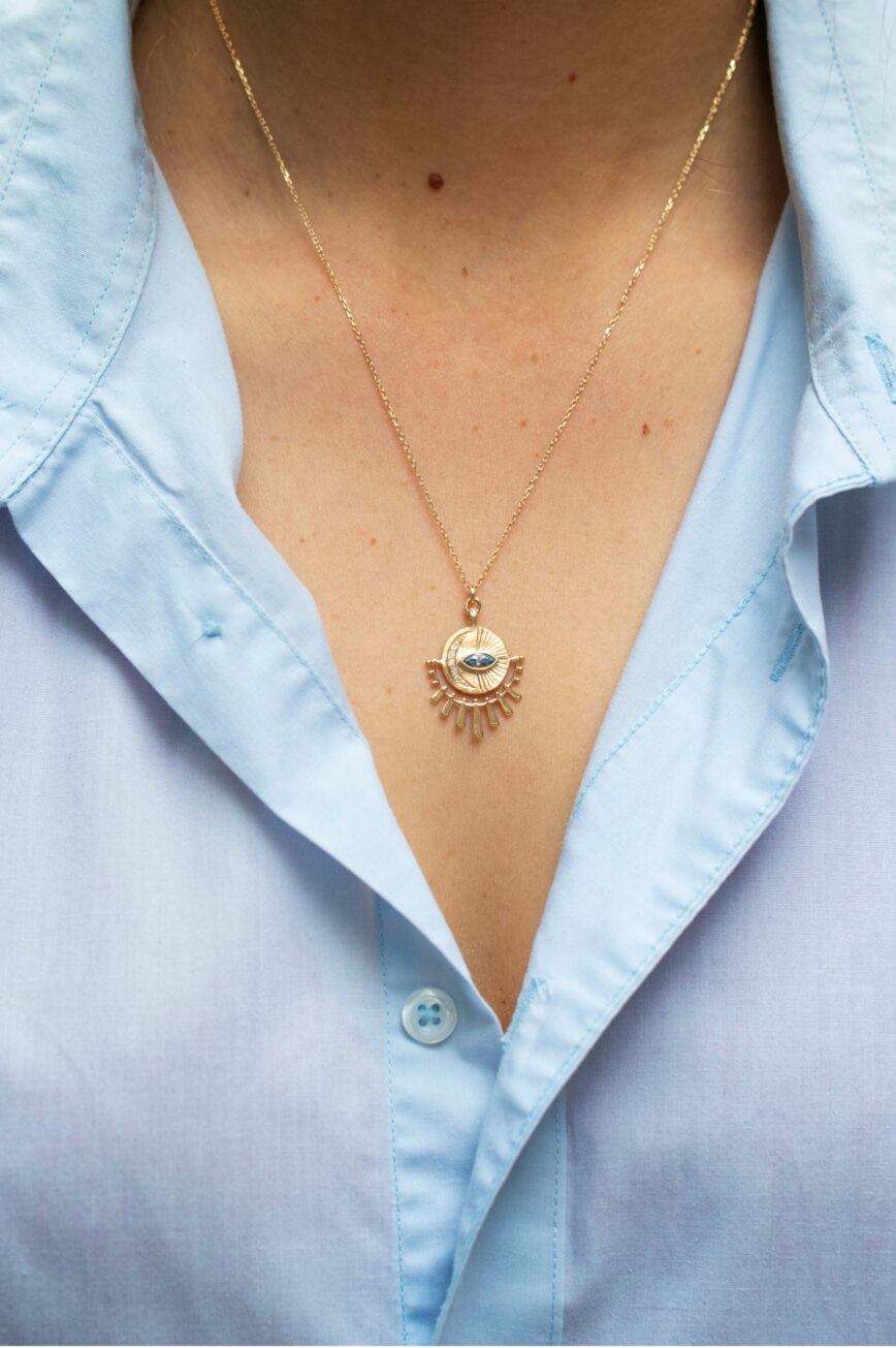 yellow gold necklace with a circular sunburst medal pendant featuring a central marquise aquamarine eye, surrounded by radiating gold sunbeams and small diamond accents