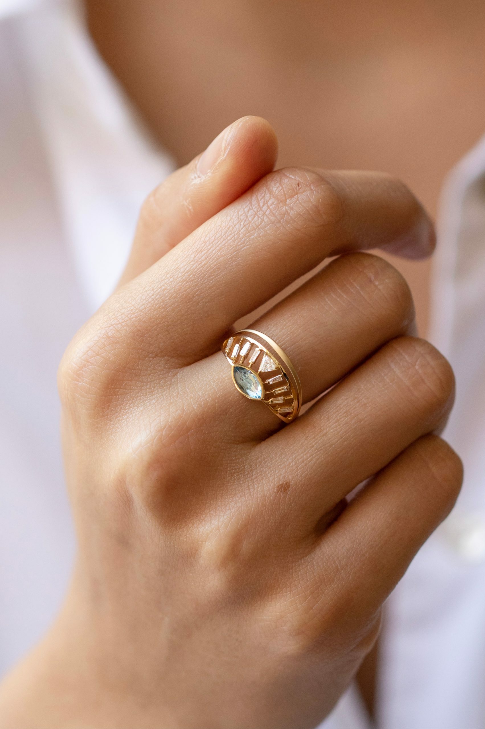 yellow gold architectural ring featuring a marquise-cut aquamarine at center flanked by baguette diamonds, set within an open cage-like crown structure