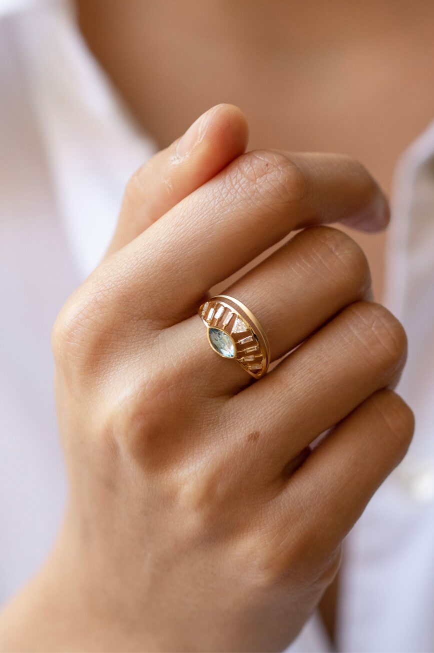 yellow gold architectural ring featuring a marquise-cut aquamarine at center flanked by baguette diamonds, set within an open cage-like crown structure