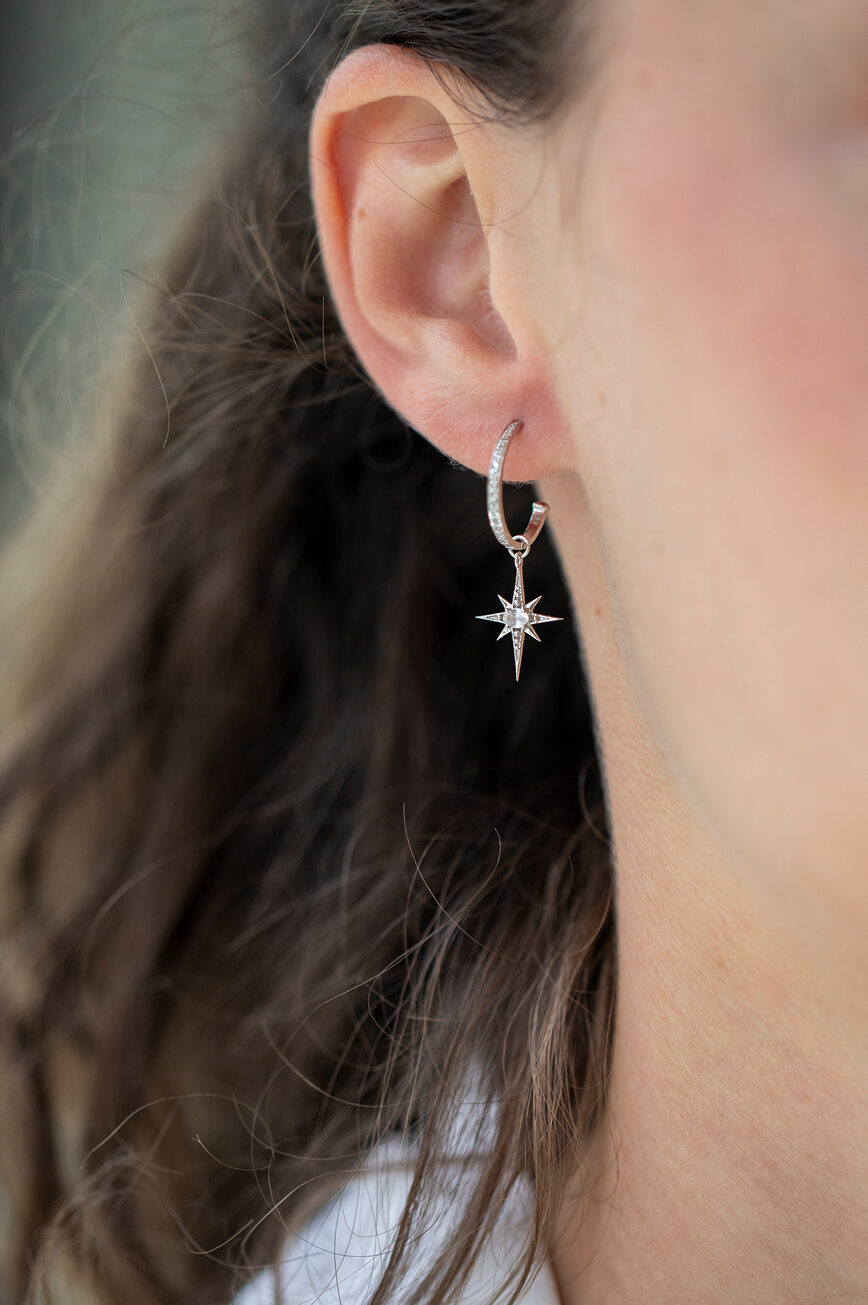 white gold single hoop earring pavé-set with diamonds, suspending a small eight-pointed north star charm set with a central white sapphire