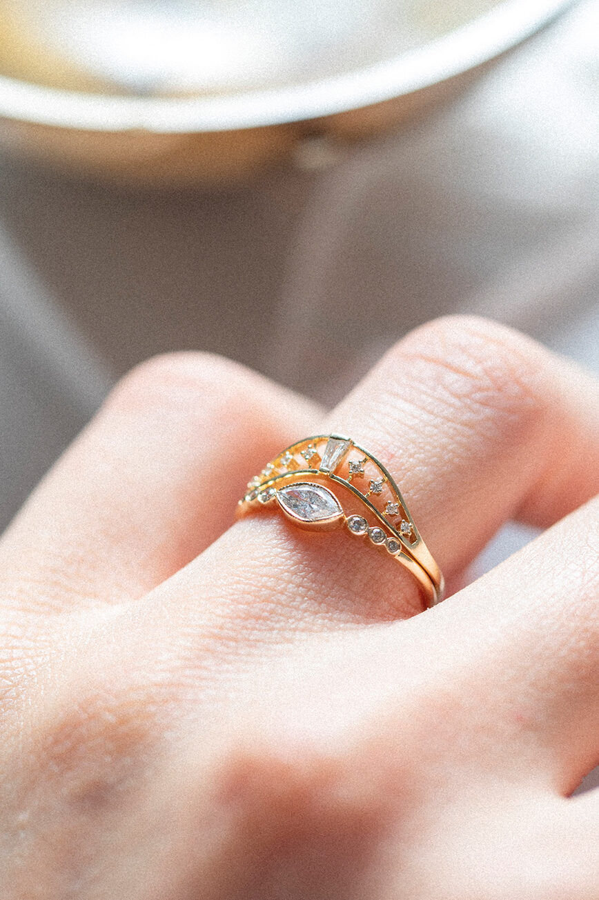 yellow gold curved ring featuring a baguette diamond at center flanked by round brilliant diamonds, set in a wave-shaped band