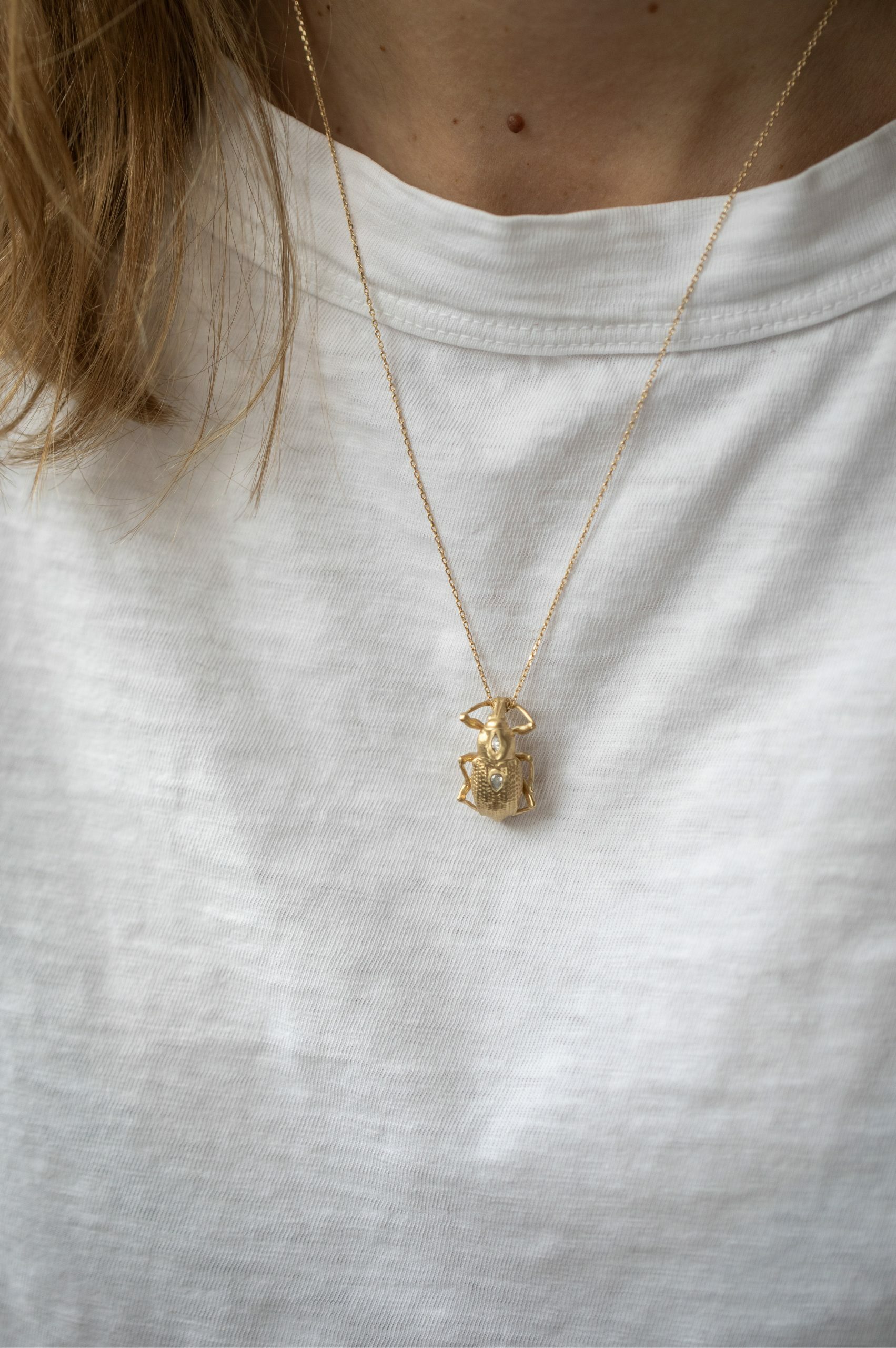 Yellow gold necklace large sculpted scarab pendant pear diamond accents held in hand Celine Daoust
