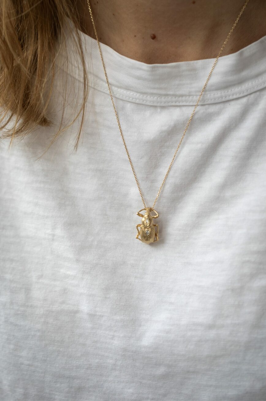 Yellow gold necklace large sculpted scarab pendant pear diamond accents held in hand Celine Daoust