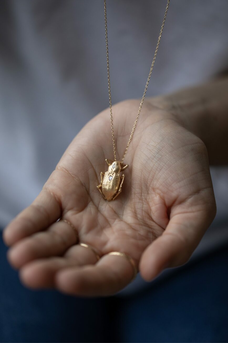 Yellow gold necklace large sculpted scarab pendant pear diamond accents held in hand Celine Daoust