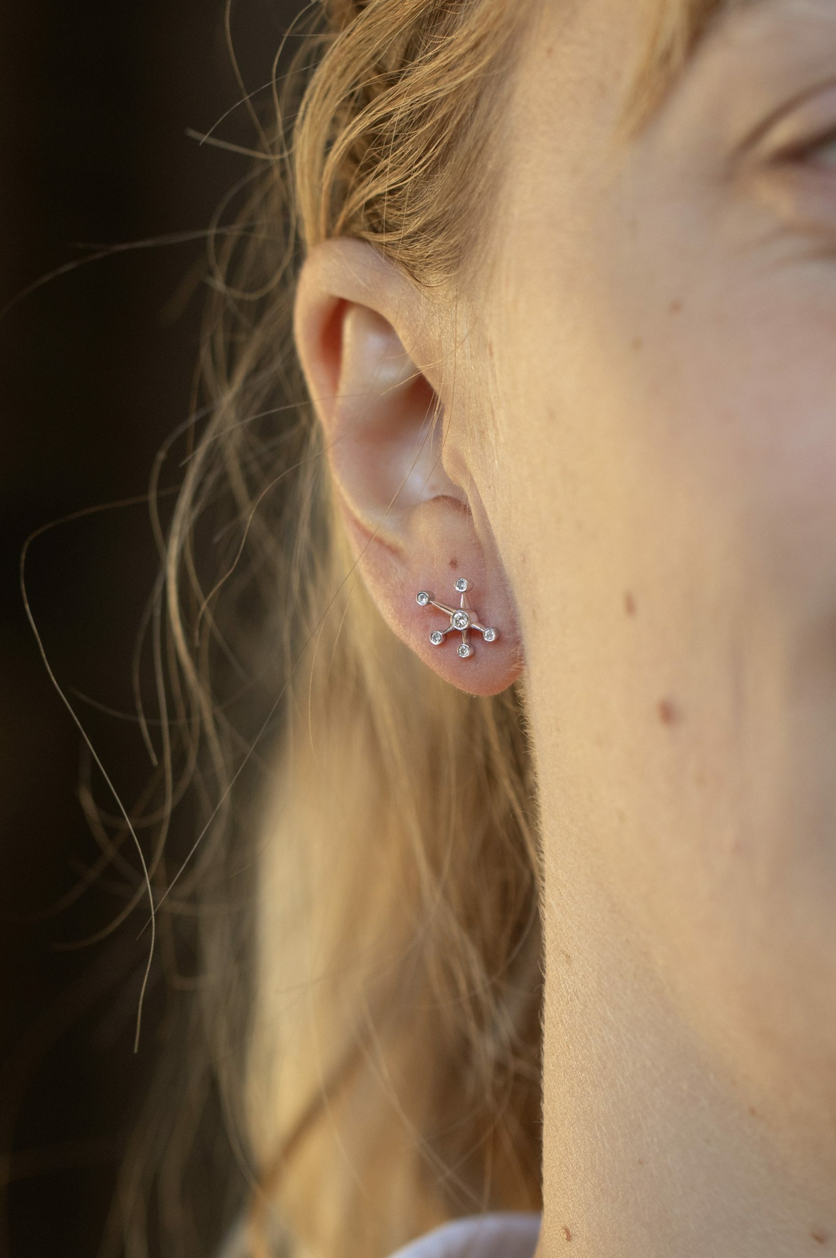 white gold stud earrings each shaped as a starburst with six radiating arms tipped with round diamonds, evoking a constellation pattern