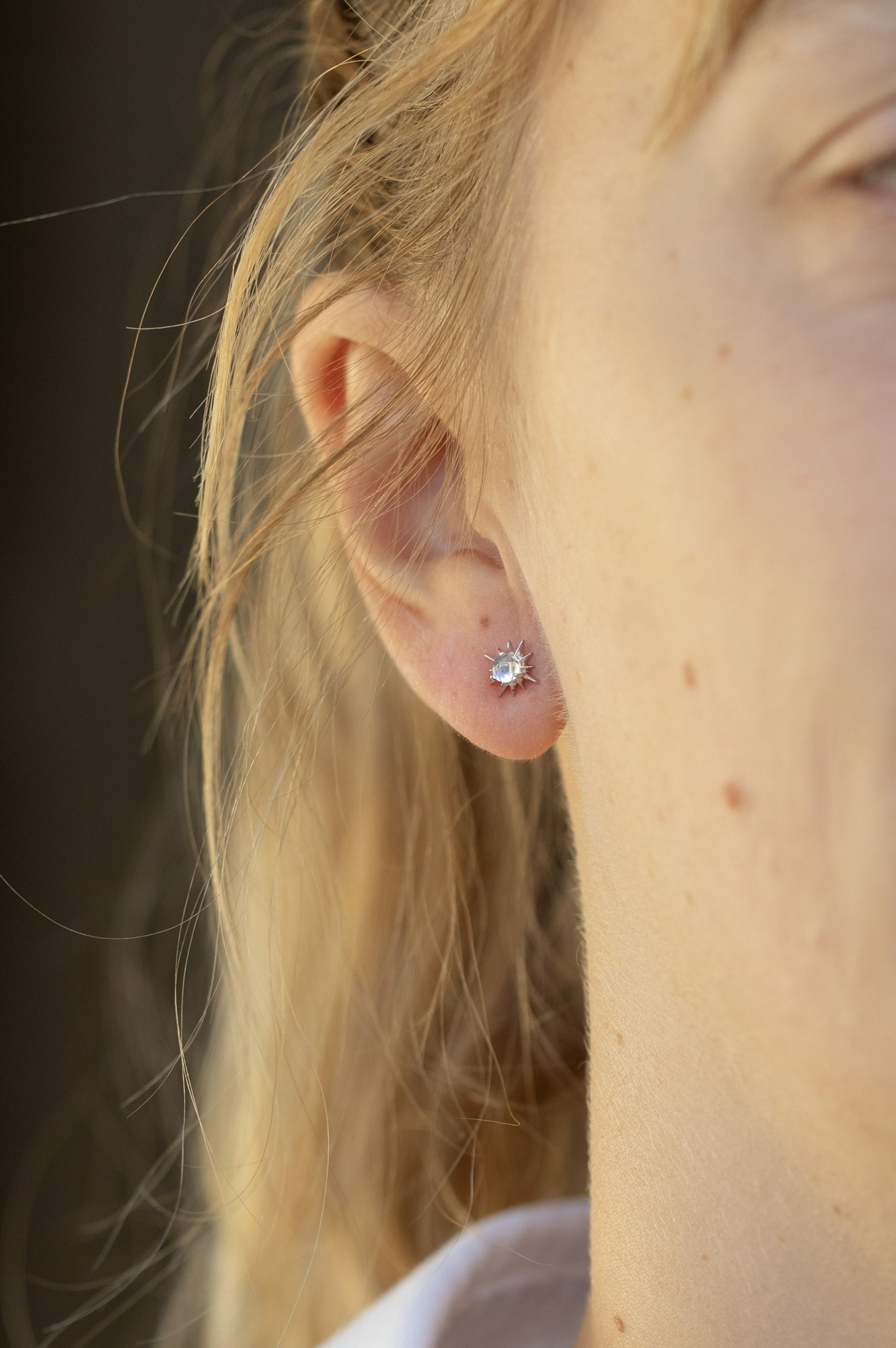 white gold stud earrings each featuring a round moonstone cabochon at center surrounded by radiating spike rays, evoking a celestial sun