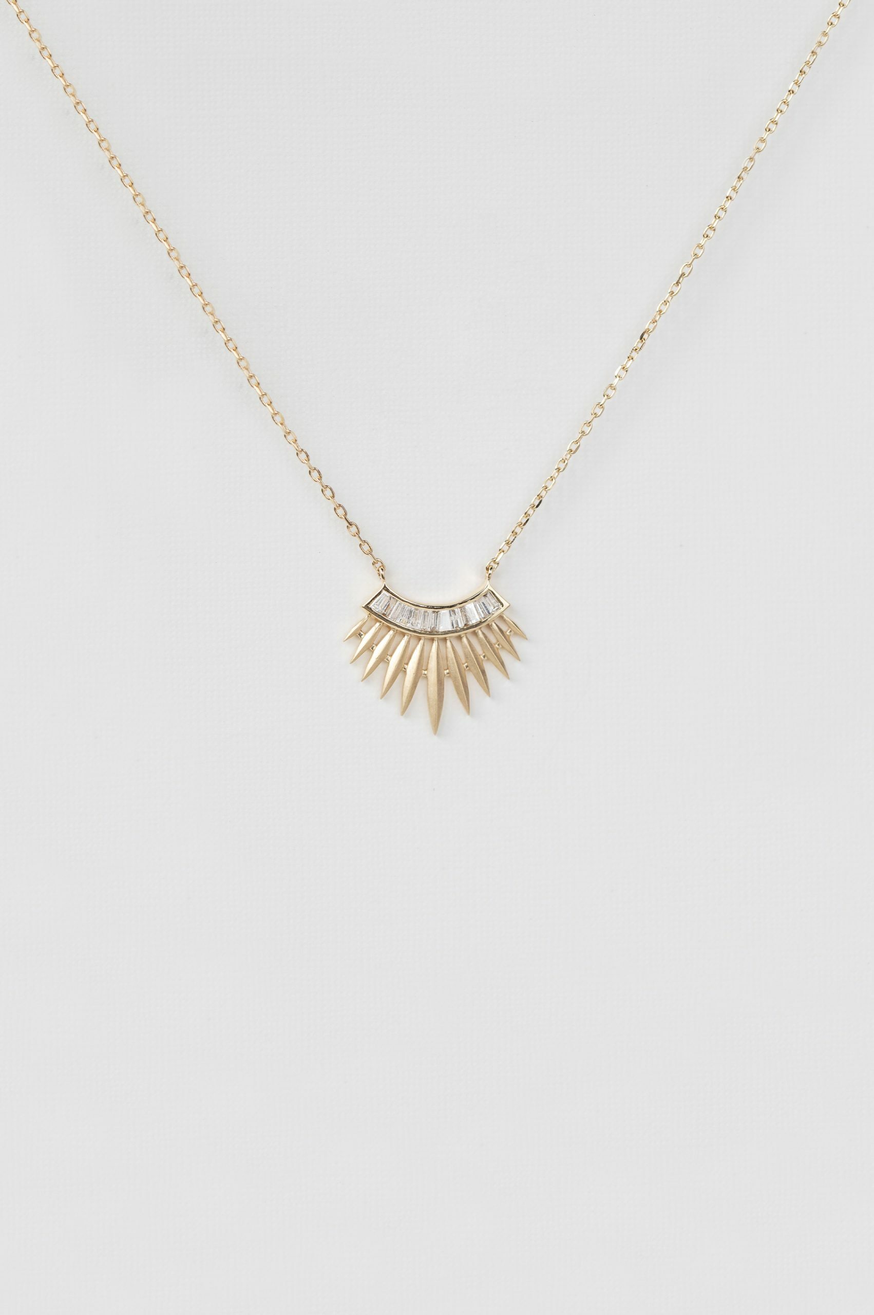 yellow gold necklace with a rising sun pendant composed of a row of baguette diamonds at center and radiating gold spike rays