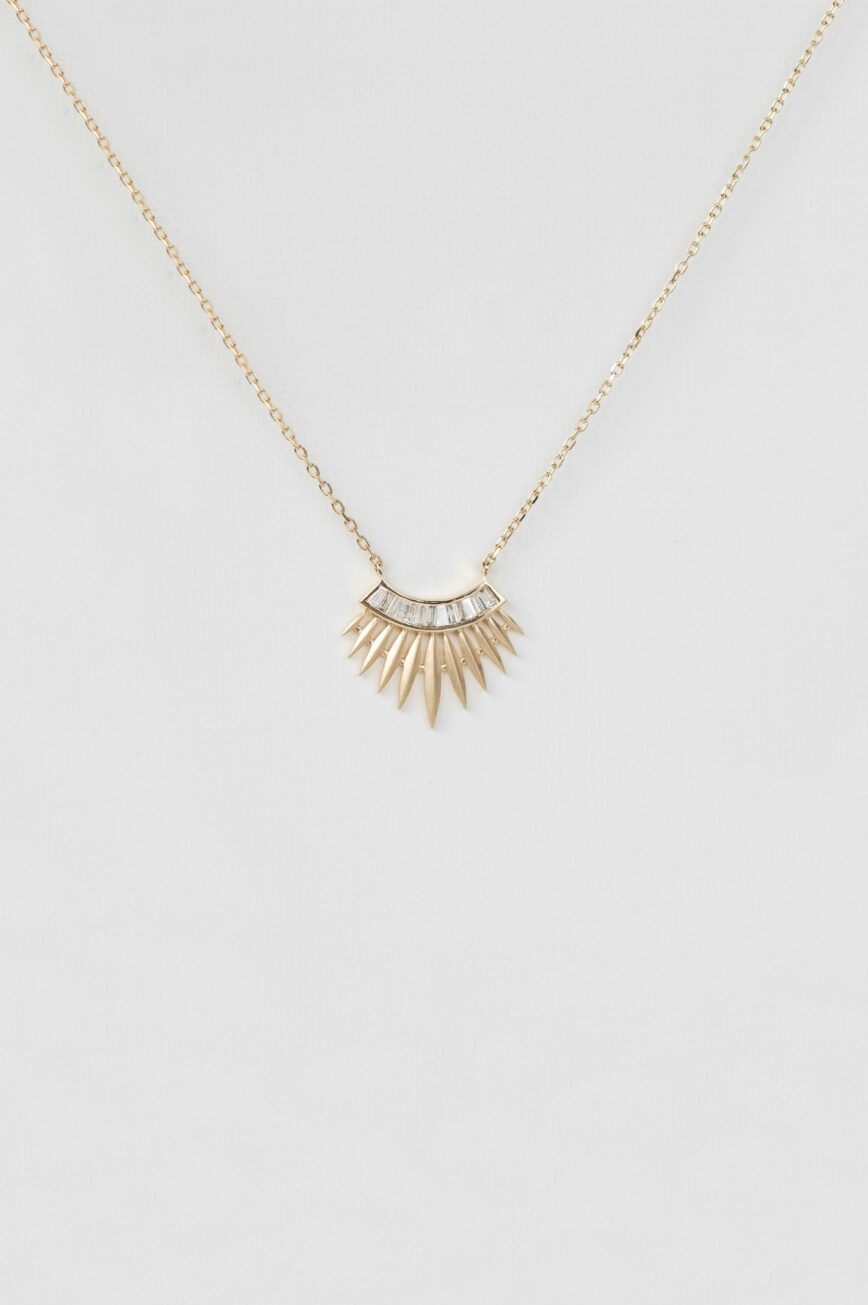 yellow gold necklace with a rising sun pendant composed of a row of baguette diamonds at center and radiating gold spike rays