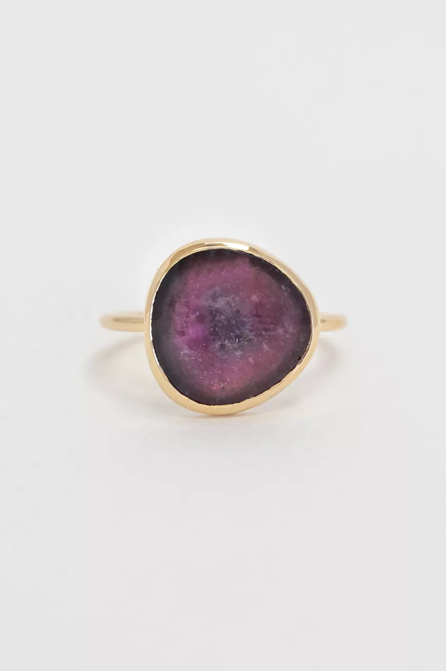 yellow gold ring with a large bezel-set slice of pink tourmaline, showcasing the stone's natural organic texture and deep magenta hues