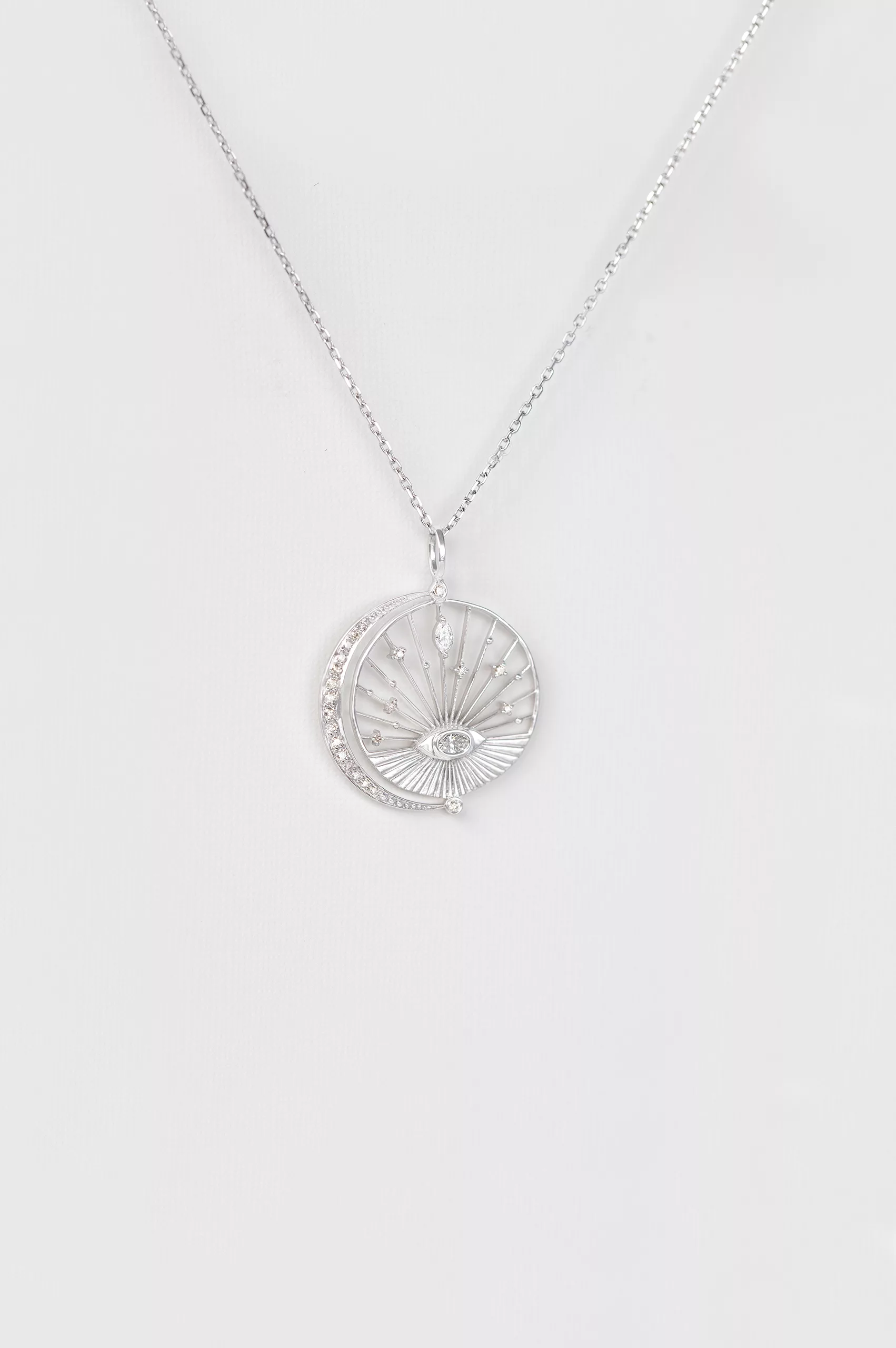 white gold circular medal necklace featuring an engraved sun eye motif at center with a crescent moon and pavé diamond accents, evoking a dreamlike celestial scene