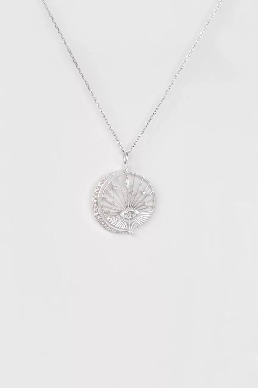 white gold circular medal necklace featuring an engraved sun eye motif at center with a crescent moon and pavé diamond accents, evoking a dreamlike celestial scene