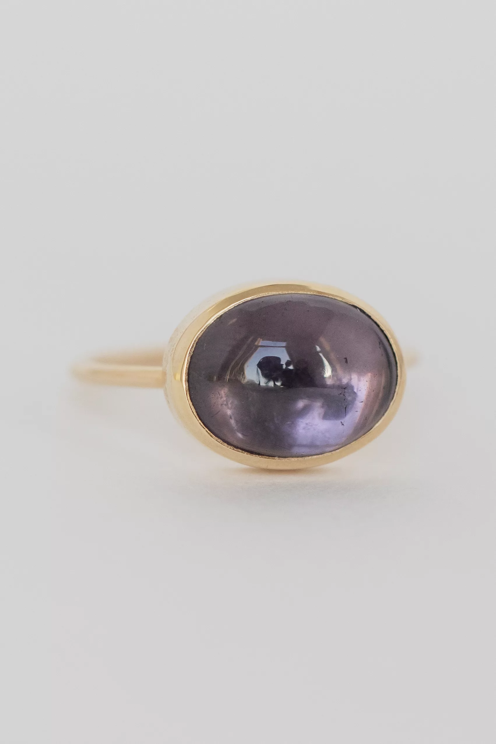 yellow gold ring featuring a large bezel-set oval cabochon of purple tourmaline in a smoky lavender hue, mounted on a slim band