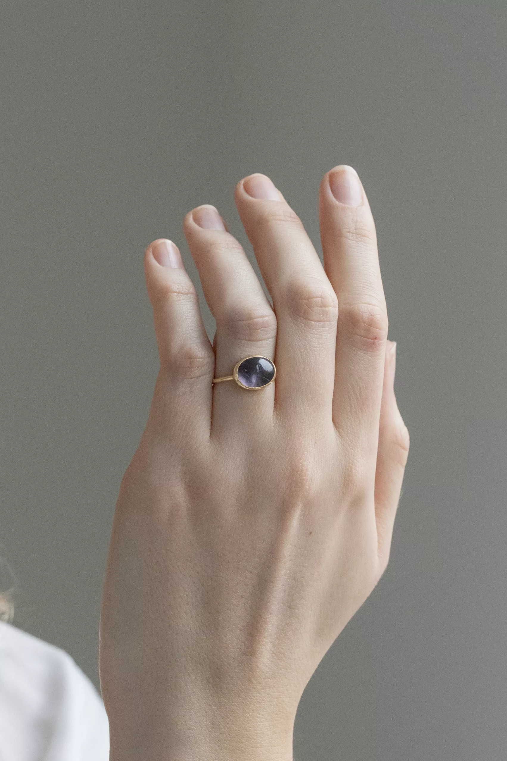 yellow gold ring featuring a large bezel-set oval cabochon of purple tourmaline in a smoky lavender hue, mounted on a slim band