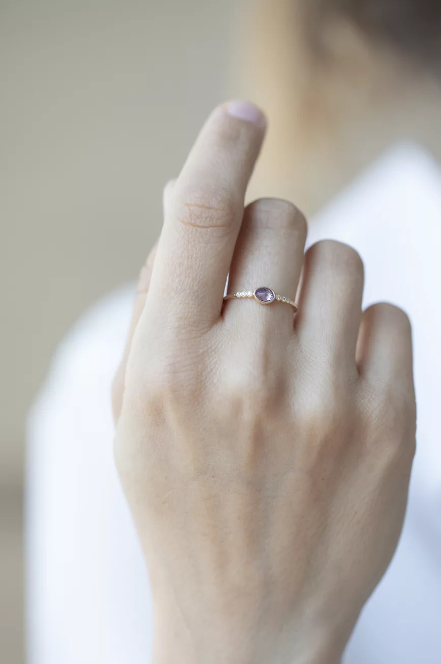 yellow gold ring with a bezel-set oval pink sapphire at center, flanked by a row of six round brilliant diamonds on a delicate band